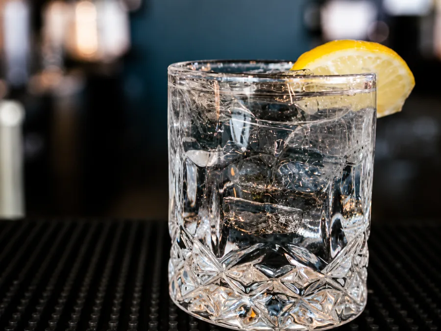A crystal-cut rocks glass with a clear cocktail, ice, and a lemon wedge on the bar at Celebration Brewing Co.