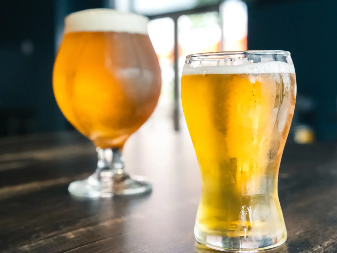 Tulip snifter and pilsner pours side-by-side on a wooden bar top