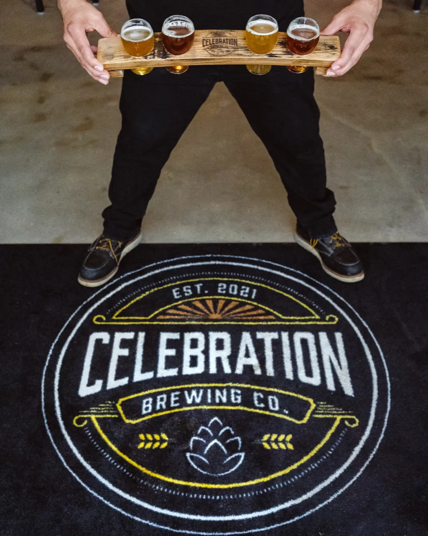 Server holding a four-glass beer flight over the Celebration Brewing Co. floor mat
