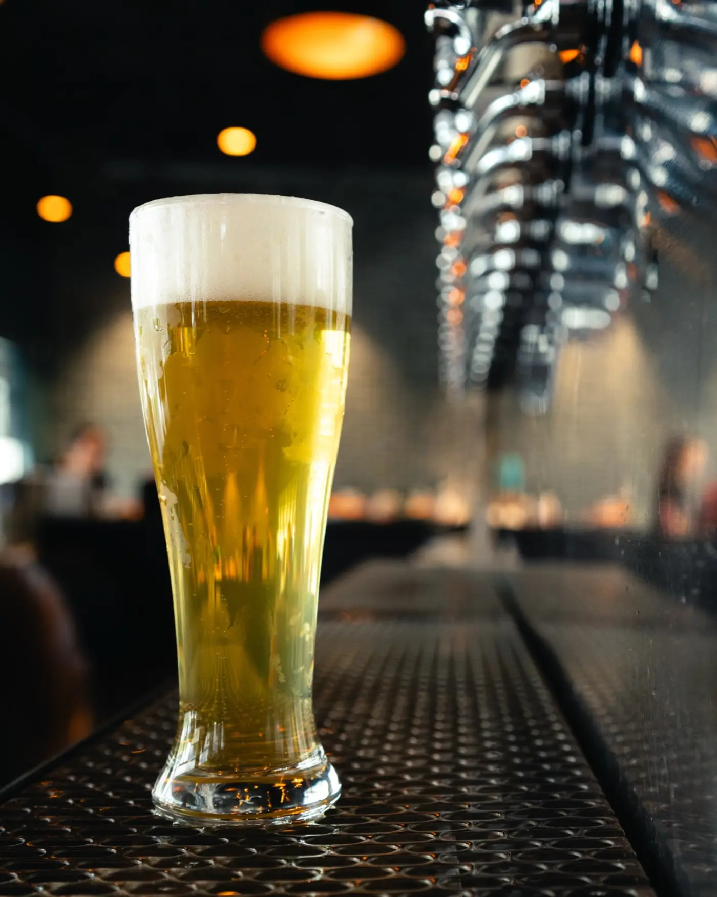 Tall pilsner of pale lager on a bar mat beneath the chrome tap line